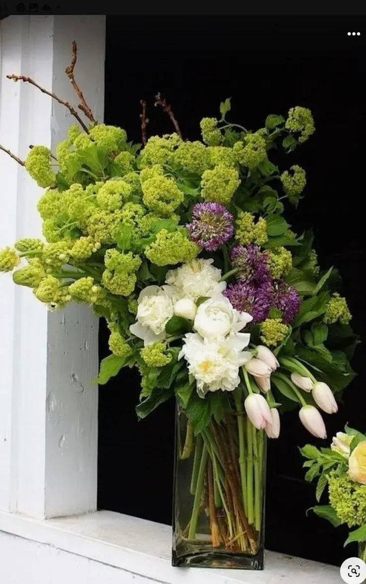 Elegant funeral bouquet with white peonies, tulips, green hydrangeas, and purple alliums in a tall glass vase – sympathy floral arrangement for funerals.