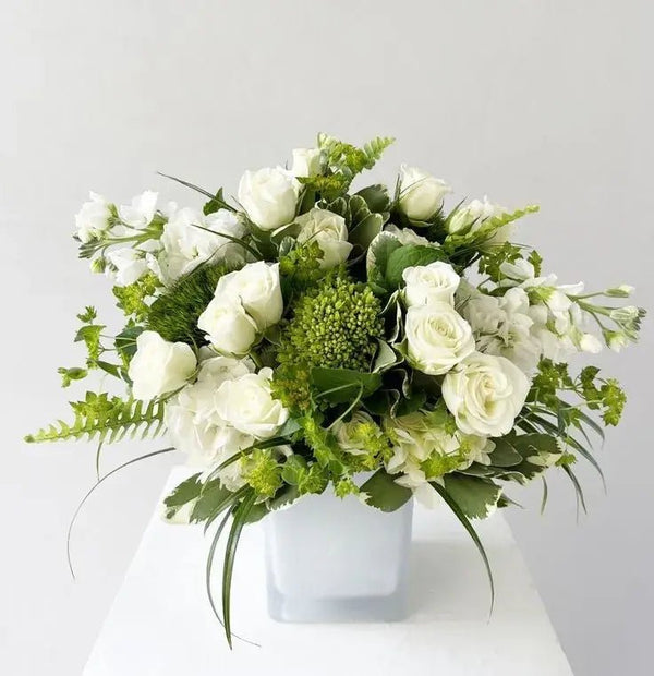 Elegant white funeral bouquet with roses, hydrangeas, and greenery in a minimalist white vase – sympathy flower arrangement for memorial services