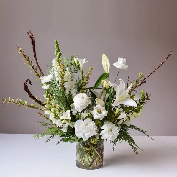 Elegant white funeral bouquet with lilies, roses, snapdragons, and chrysanthemums in a glass vase, symbolizing peace and remembrance.