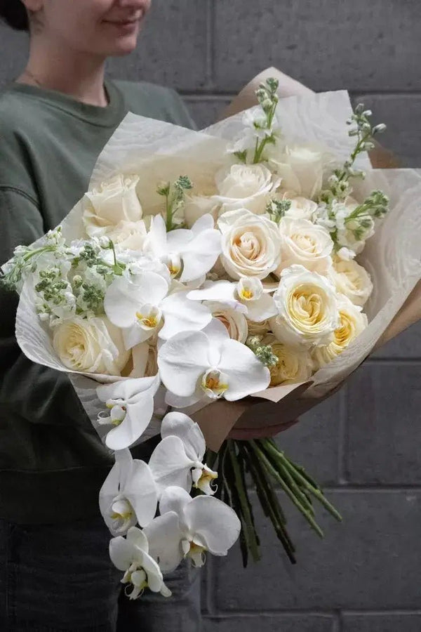 Refined funeral bouquet with cascading white orchids and cream roses, wrapped in neutral-toned paper – a graceful floral tribute for funerals and memorial services