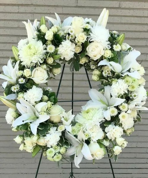 Elegant white funeral wreath with lilies, roses, chrysanthemums, and daisies on a stand – serene floral tribute for funerals and memorial services.